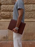 brown leather MacBook sleeve carried in hand, lifestyle